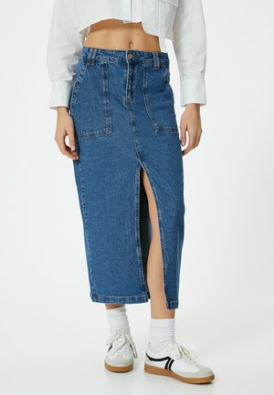 Jupe midi en denim avec fente avant, couleur bleu clair, deux poches avant et taille haute, assortie à des baskets blanches et des chaussettes.