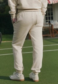 Beżowe spodnie dresowe z elastycznym pasem, ściągaczami przy kostkach i kieszeniami po bokach. Skąpane w białych trampkach z gumową podeszwą.