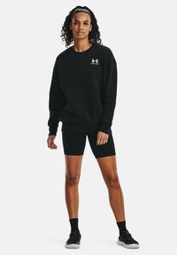Sudadera negra con cuello redondo, puños y dobladillo acanalados; combinada con pantalones cortos de ciclismo negros. Presenta un logo blanco en el pecho y un tejido texturizado.