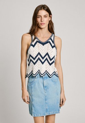 Top in cotone bianco e blu navy con motivo a zigzag, orlo scallop e spalline sottili, abbinato a una gonna in denim azzurro chiaro.