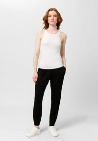 Top blanco sin mangas con tirantes finos, combinado con pantalones jogger negros de corte holgado y zapatillas blancas. Tela suave, diseño simple, aspecto casual.