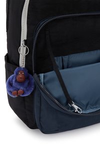 Sac à dos noir avec fermeture éclair argentée métallique et une poche d'accent bleue. Porte-clé en forme de singe violet en peluche attaché, avec des mains et un visage marron.