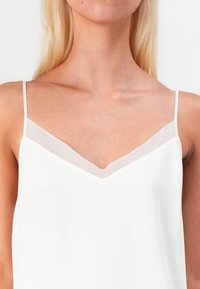 Weißes Camisole mit dünnen Trägern, einem V-Ausschnitt und durchsichtigen Akzenten entlang des Ausschnitts und Saums, mit einer glatten, leichten Textur.