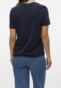 Granatowa koszulka z krótkim rękawem o klasycznym dekolcie, gładka w dotyku i luźna. Połączona z jasnoniebieskimi dżinsami.
