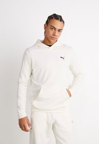 Sudadera blanca hecha de tela suave, con un bolsillo tipo canguro, logo bordado en el pecho y capucha con cordón. Combinada con pantalones a juego.
