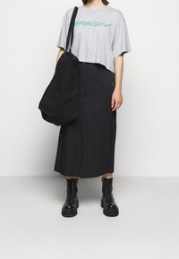 Grå kortärmad t-shirt med grön grafik, svart midi kjol, svart tote-väska och kraftiga svarta snörstövlar med en texturerad yta.