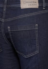 Mörkblå denimjeans har en enda bakficka med vit sömnad och en läderetikett märkt "Street One" ovanför midjan.