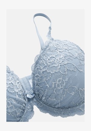 Lichtblauwe kanten beha met bloemmotieven, verstelbare bandjes en een klein decoratief strikje tussen de cups op een effen achtergrond.