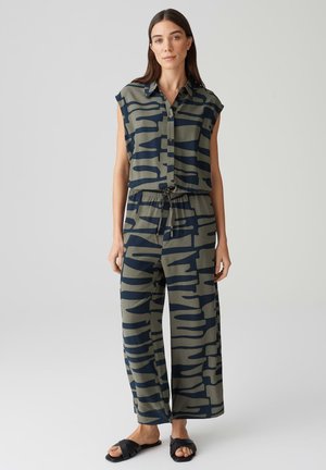 Ensemble deux pièces à motif vert et marine composé d'une chemise sans manches avec des boutons et un pantalon large avec une ceinture élastique. Sandales noires.