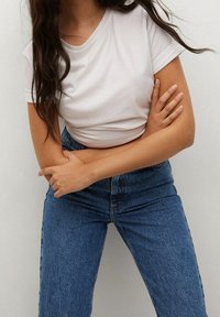T-shirt blanc en coton avec un col rond, associé à un jean en denim bleu taille haute. Texture lisse, coupe ajustée et manches retroussées.