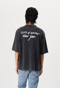Sort oversized t-shirt med korte ærmer, med hvid tekst: "CITY of Dreams" og "New York" på ryggen. Teksten i graffiti-stil.