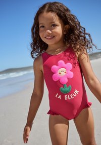 Rood eendelig badpak met een roze bloemmotief, geborduurde accenten en ruches bij de benen. Tekst: "LA FLEUR."