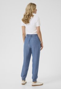 Joggers de denim azul claro con cinturilla elástica y dobladillos ajustados. El modelo lleva una camiseta blanca de canalé, mostrando un diseño simple.
