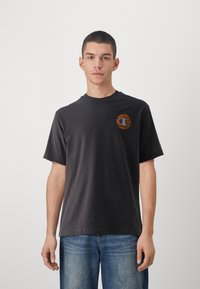Dark gray cotton t-shirt with short sleeves. Features a colorful circular logo on the left chest. Simple design; crew neckline.