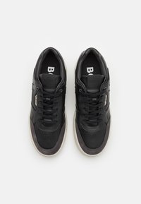 Černé tenisky s hladkým koženým svrškem, šedými semišovými akcenty, kulatou špičkou, plochými tkaničkami a gumovou podešví. Značka viditelná na stélce.