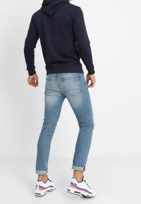 Sudadera con capucha azul marino, vaqueros ajustados de color azul claro y zapatillas blancas con detalles en rosa y azul. La sudadera tiene un bolsillo canguro y una capucha ajustable.