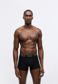 Black boxer briefs with a soft fabric, featuring a logoed elastic waistband. Smooth texture, fitted design, and mid-thigh length.