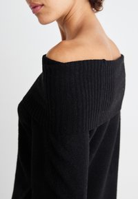 Svart off-the-shoulder genser med ribbet halslinning. Materialet er mykt, med en avslappet passform og glatt tekstur.