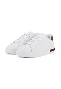 Un paio di sneakers bianche a bassa altezza con lacci bianchi, branding sottile e dettagli in maroon sul tallone, su uno sfondo bianco.