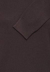 Manche de pull en maille marron foncé avec détail de poignet côtelé sur fond de tissu assorti.