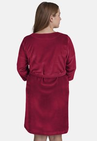 Accappatoio in fleece di un rosso intenso, con vestibilità comoda, maniche lunghe e cintura in tessuto, caratterizzato da una superficie morbida e liscia.