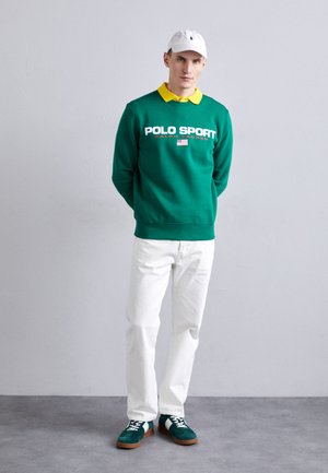 Grøn sweater med "POLO SPORT" tekst, gul krave, hvide jeans og grønne ruskindsneakers med hvide snørebånd og brune såler. Hvid kasket.