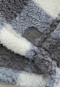 Couverture douce et moelleuse en gris et blanc avec une étiquette cousue portant l'inscription "ICI VIENNE L'ÉTOILE" sur un tissu texturé.