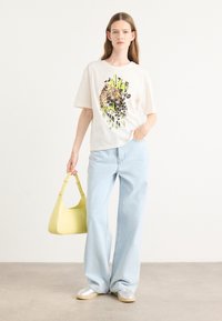 Hvit oversize t-skjorte med leopardmønster og grønn grafikk, kombinert med lyseblå vide jeans og en gul lærveske.