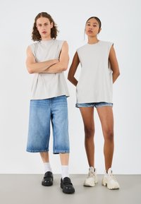 Svetlé šedé tielka bez rukávov, voľné denimové šortky, čierne slip-on topánky a robustné tenisky; čisté línie a jemné textúry.