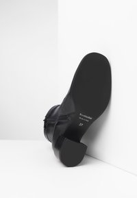 Scarpa ankle in pelle nera con tacco a blocco, dettaglio con zip e suola in gomma testurizzata. Contrassegnata con informazioni sul marchio e sulla taglia.