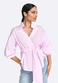 Camicia avvolgente rosa con scollatura a V profonda, maniche oversize e vita legata. Realizzata in tessuto di cotone con una texture liscia.