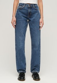Vaqueros rectos de color azul oscuro con cintura alta, que cuentan con un diseño clásico de cinco bolsillos, costuras en contraste en color naranja y ligero desgaste.