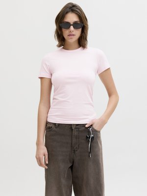 Femme portant des lunettes de soleil noires étroites, un t-shirt rose clair à manches courtes et un jean ample gris foncé avec un porte-clés à la boucle de ceinture.
