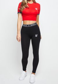 Röd kort topp med korta ärmar och svarta leggings med elastisk midja och logga. Kompletteras med vita sneakers.