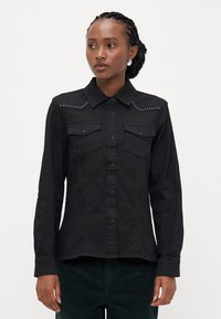 Zwarte denim shirt met knoopsluiting, twee borstzakken en studded accenten op de schouders. Lange mouwen met knoopsluitingen, textiel met structuur.