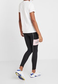 Zwarte leggings met een roze horizontale strook met de tekst "Candy", witte zijstrepen, gecombineerd met een eenvoudig wit t-shirt en kleurrijke sneakers.