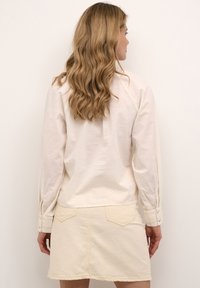 Cremefarvet skjorte med lange ærmer og knapmanchetter, parret med en beige denimnederdel med to baglommer og dekorativ syning.