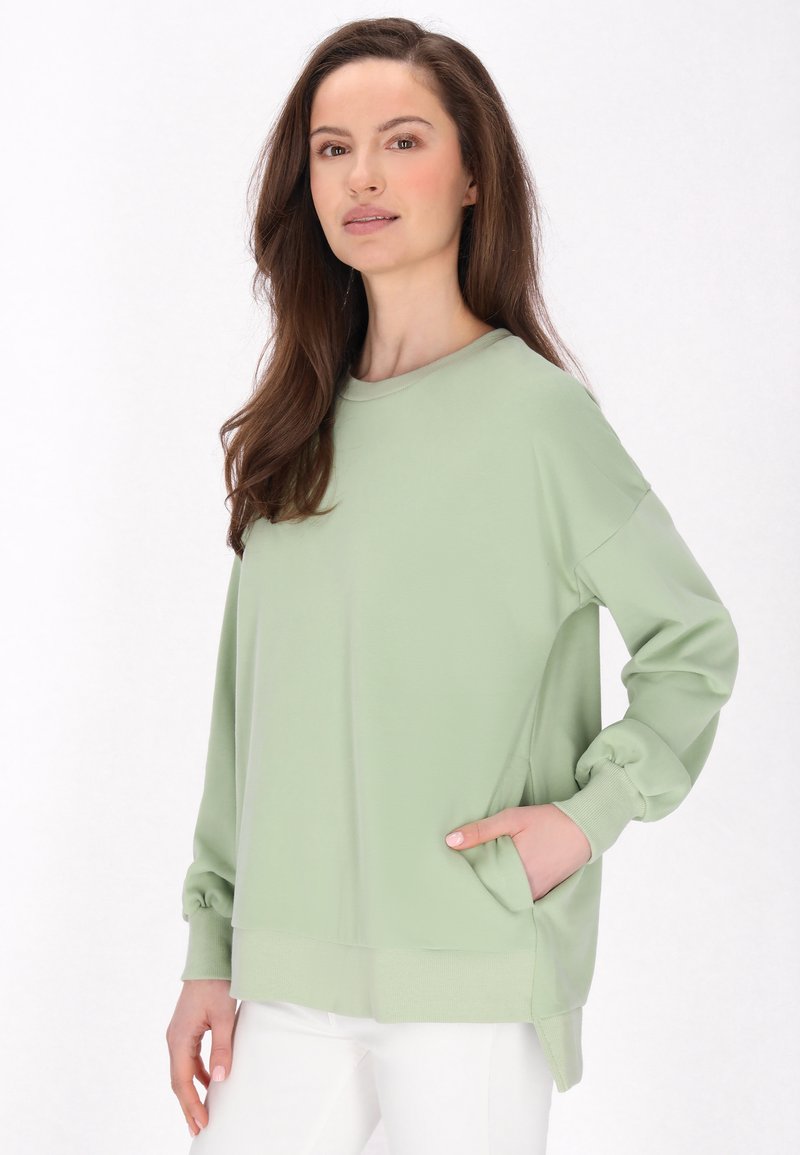 Felpa a maniche lunghe verde chiaro con vestibilità comoda, scollo rotondo, polsini a costine e tasche laterali. Tessuto morbido e texture liscia.