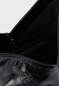 Melna ādas soma ar spīdīgu faktūru, atvērta, lai parādītu melnu auduma oderi un iekšpusē rāvējslēdzēja kabatu.