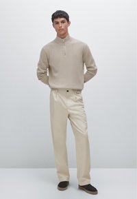 Beige ribbed sweater with half-zip collar, paired with cream pleated trousers and dark footwear. Simple, structured design and neutral colors.