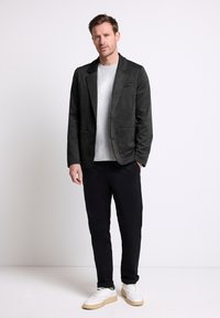 Czarna żakiet o teksturze z dwoma przednimi kieszeniami, w połączeniu z szarym t-shirtem i czarnymi spodniami. Białe sneakersy podkreślają stroje.