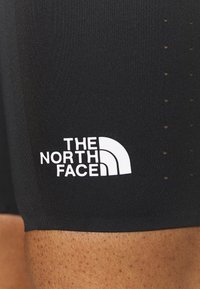 Czarne sportowe szorty wykonane z elastycznego materiału, z małymi otworami wentylacyjnymi i wyraźnym białym logo "The North Face."