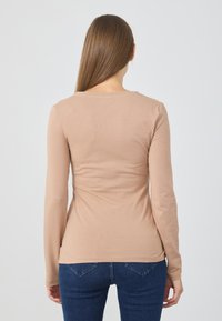 Maglietta a maniche lunghe, aderente, in tessuto a costine di un beige chiaro con scollo rotondo. Abbinata a jeans blu scuro.