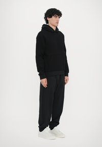 Felpa nera in pile con tasca a marsupio, abbinata a pantaloni neri larghi e sneakers bianche. Design semplice con polsini e orlo a coste.