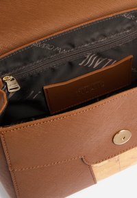 Borsa in pelle marrone testurizzata con una tasca con cerniera all'interno. Presenta una chiusura con bottone a pressione e un compartimento color cuoio con marchio impresso a rilievo.