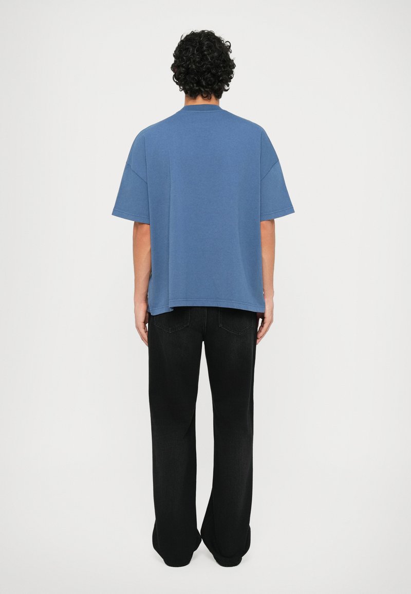 Blue cotton t-shirt with dropped shoulders and a relaxed fit, paired with black straight-leg jeans. Simple design, no visible patterns or accents.