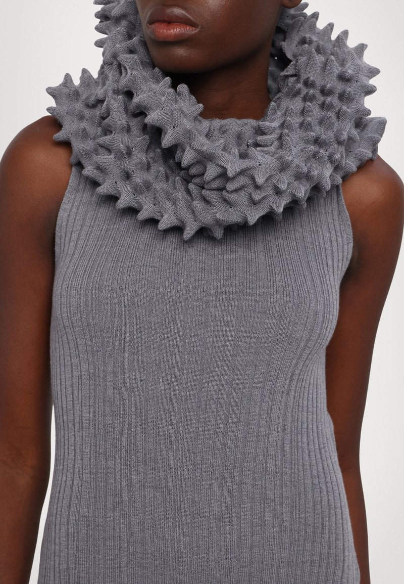 Scarf grigia a collo rotondo lavorata a maglia con dettagli in rilievo e arricciati, abbinata a un top grigio senza maniche a costine. Tessuto liscio, colore solido.