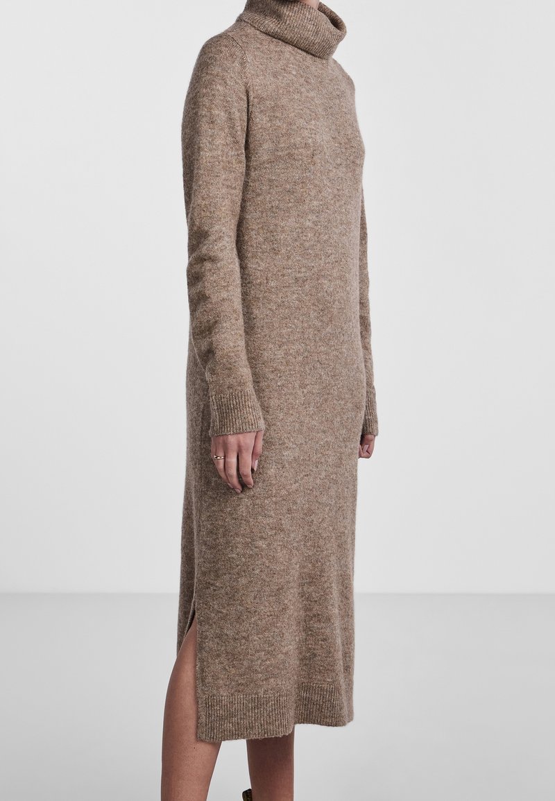 Robe en tricot à col roulé couleur marron clair, avec des manches longues, des fentes latérales et des bords côtelés aux poignets et à l'ourlet. Tissu doux et texturé.