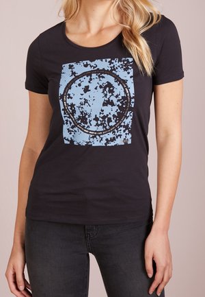 Kvinde iført en sort t-shirt med et blåt abstrakt firkant- og cirkeldesign, der står "LOVE TO LOVE" i et gentaget mønster.