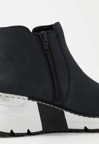 Stivaletto nero alla caviglia con zip laterale, caratterizzato da una tomaia testurizzata, suola a zeppa bianca e nera a contrasto e cuciture dettagliate.